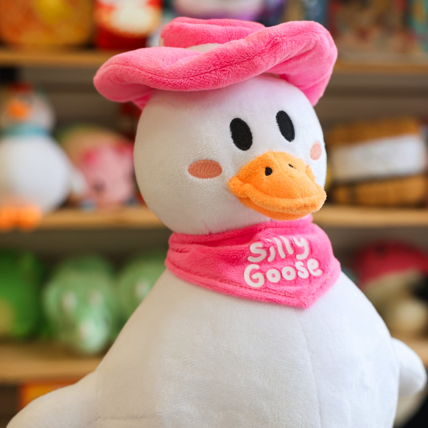 Plush toy goose with pink hat and scarf labeled 'Silly Goose' in a store setting