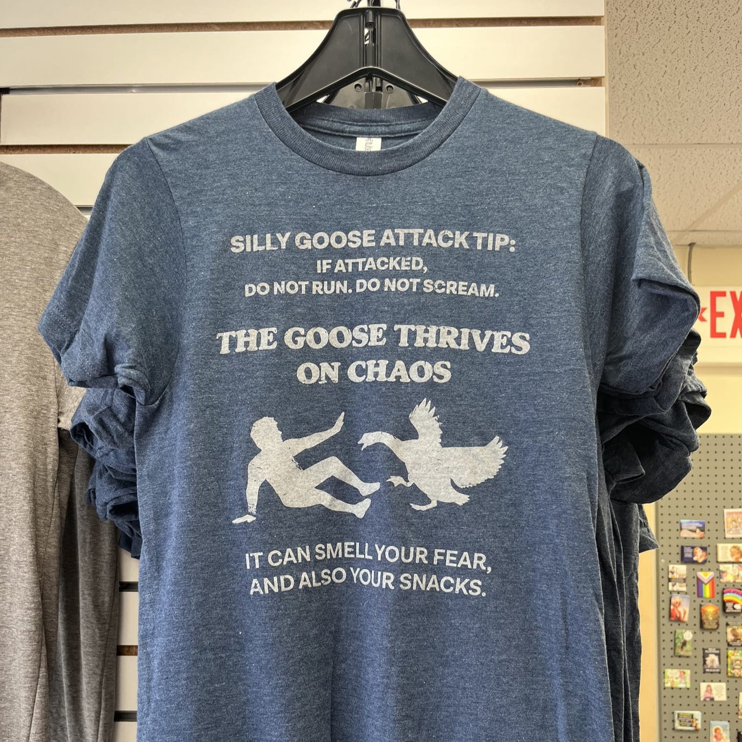 Blue t-shirt with humorous text and graphics on a hanger against a store background