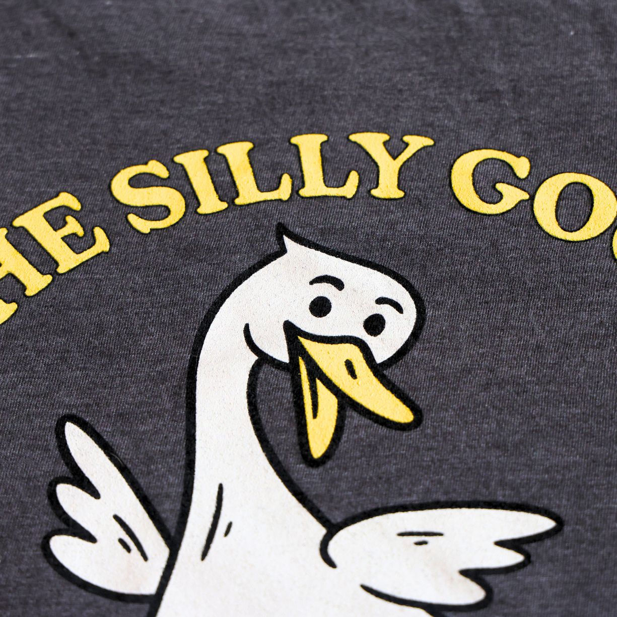 Dark gray t-shirt with cartoon goose and 'The Silly Goose' text in yellow.