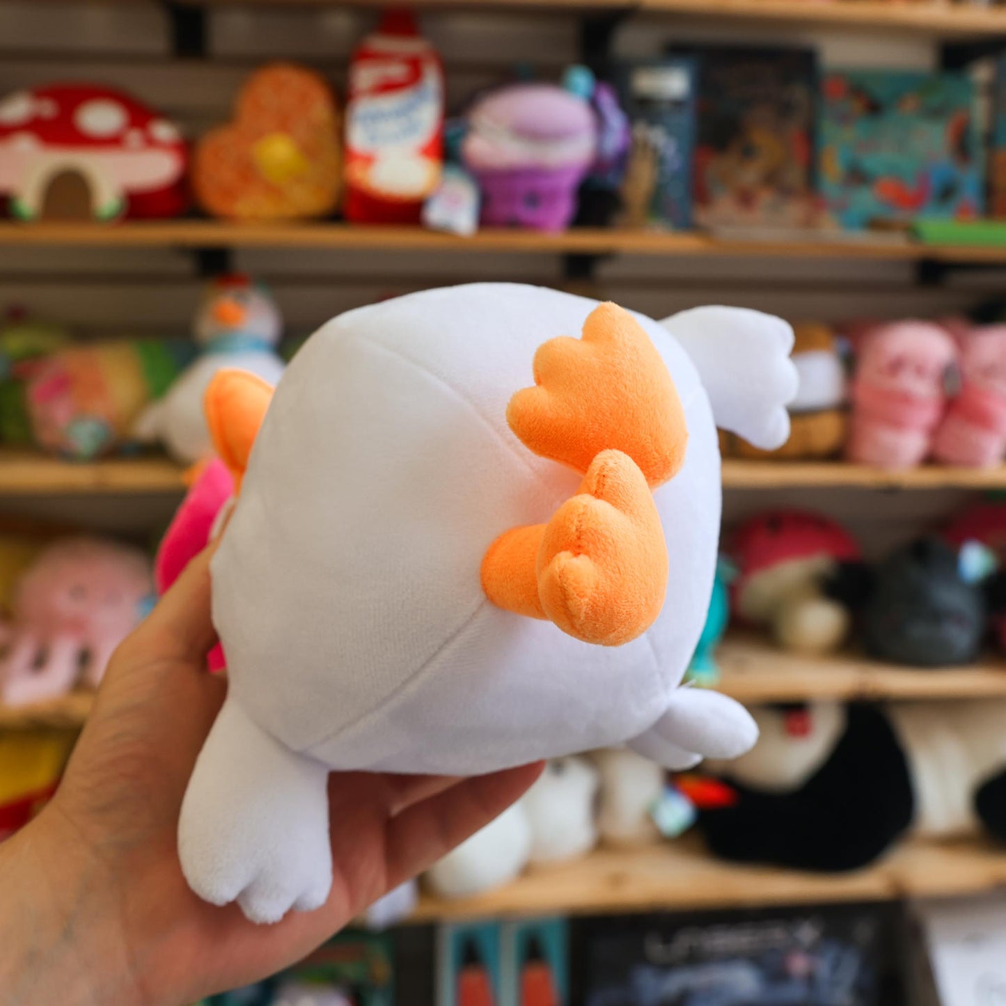 Plush toy resembling a goose held in front of a shelf with various toys.