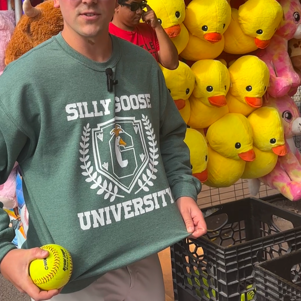 Man holding a yellow ball in front of a wall of stuffed animals, including teddy bears and rubber ducks.
