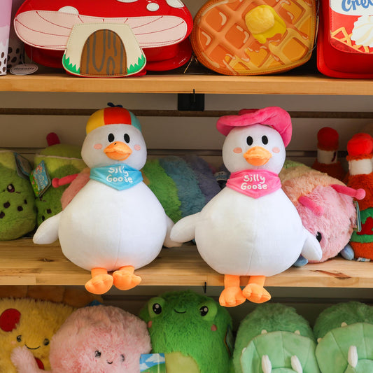 Two plush goose with colorful hats on a shelf with other toys.
