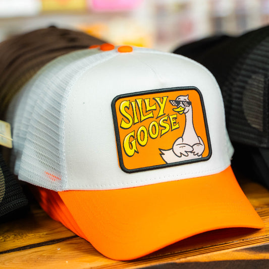 Orange and Silly Goose white cap with 'Silly Goose' logo on a wooden surface